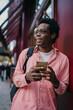 © BullRun - African freelancer holding smartphone and looking to side with calm smile, leaning on wall, symbolizing awareness, digital readiness and confidence in freelance path.