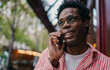 © BullRun - Mid-shot of African man smiling while talking on phone outdoors, confident and expressive, illustrating clarity, connection and personality in remote freelance tech culture.