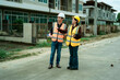 © ArLawKa - Asian male and female engineers and architects discuss at a construction site; professional colleagues wearing safety vests collaborate on an industrial-style housing project.