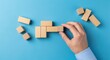 © TANZIM22 - Hand carefully placing final wooden block piece completing a structure emphasizing problem solving and strategic business development against a vibrant blue background