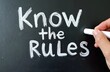 © Vadym - Blackboard with Know the Rules written in chalk. Hand holding chalk, writing or erasing on surface. Concept for guidance instruction and compliance in business or education.
