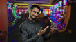 © Krakenimages.com - Young man smiling indoors at a vibrant casino with slot machines, holding a mini shopping cart, embodying modern leisure and entertainment.