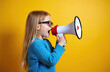 © Viktor - Little girl with glasses shouts into megaphone. She wears blue sweater against bright yellow background. This image is great for announcements, marketing, or kids education concepts with copy space.