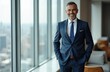 © Viktor - Smiling middle aged man in navy suit stands hands in pockets. Confident businessman at office window with city view. Pro executive looks happy and successful. Career growth.