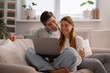 © My Ocean studio - Smiling couple enjoying shared screen time on the couch, cozy home entertainment with laptop in a bright living room.