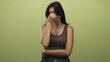 © Krakenimages.com - Young hispanic woman pinches nose with hand in studio while wearing brown tank top and blue jeans; disgust.