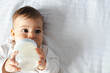 © SISMIZ - Cute Baby Drinking Milk from Bottle on White Bedding
