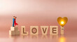 © PhotoArtHub - Miniature couple figurine, wooden block letters spelling love, and a golden heart on a pink background, representing affection and Valentine's Day
