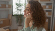 © Krakenimages.com - Woman holding smartphone to ear, smiling while speaking among parcel boxes in an office building; friendly service.
