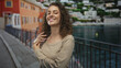 © Krakenimages.com - Woman touches her curly hair and smiles with eyes closed on a seaside street promenade by metal railing and calm water; carefree joy.