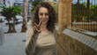 © Krakenimages.com - Woman showing v sign with fingers near face on sunlit city street beside stone building wearing beige top and curly hair; playful mischief.