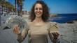 © Krakenimages.com - Woman holding fan of cash and a small wooden house on a seaside street; financial success confidence.