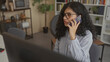 © Krakenimages.com - Woman holding smartphone to ear at office desk, wearing glasses and striped shirt while speaking on phone; work focus productivity.
