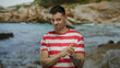 © Krakenimages.com - Young man in striped shirt gestures with hands against a blurred seaside backdrop, conveying a relaxed and engaging atmosphere.