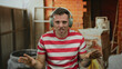 © Krakenimages.com - Man wearing headphones in striped shirt at construction site, expressing emotions with hand gestures showcasing tattoos on arm.