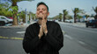 © Krakenimages.com - Man wearing black robe standing on urban street with palms in background showing emotion with eyes closed and hands near face.