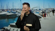© Krakenimages.com - Man smiling in priest attire holding bible at a marina with boats in the background, conveying a sense of contemplation and joy by the seaside.
