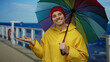 © Krakenimages.com - Young man in yellow raincoat holds colorful umbrella on a cruise ship deck by the sea, smiling under a blue sky wearing a red beanie.