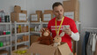 © Krakenimages.com - Young man in red volunteer shirt organizes stuffed animals in donation room with shelves filled with food and boxes.