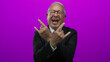 © Krakenimages.com - Senior man in a business suit making rock hand gestures with a playful expression against a bright pink background wall.