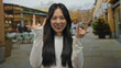 © Krakenimages.com - Young chinese woman makes a rock gesture with her fingers while smiling on a sunny restaurant terrace in a lively outdoor street setting.
