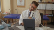 © Krakenimages.com - Young hispanic man in white coat wearing stethoscope holds phone and consults notes in a building; professionalism.