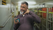 © Krakenimages.com - Middle aged man with grey beard holding blue enamel mug and making call gesture in building corridor while smiling; friendly casual playful.