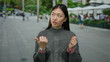 © Krakenimages.com - Woman gesturing on urban street wearing gray sweater showcasing city life and fashion in an asian setting with a blend of culture and style.