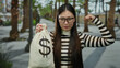 © Krakenimages.com - Confident woman in striped top holding dollar bag and flexing arm on urban street, showcasing strength and success.
