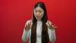 © Krakenimages.com - Woman gesturing calmly against red background, emphasizing serenity, wearing white clothing, isolated asian female, expressing peaceful message, suggesting calm communication.
