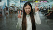 © Krakenimages.com - Woman smiling while making peace signs in a bustling airport terminal, suggesting a joyful travel experience in a dynamic indoor setting.
