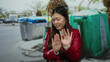 © Krakenimages.com - Woman in a red jacket with a disgusted expression stands outdoors near city waste bins on urban street.