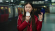 © Krakenimages.com - Woman talking into microphone at indoor train station in china wearing red jacket with blurred train in background.