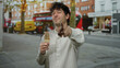 © Krakenimages.com - Man enjoying ice cream outdoors with a playful gesture on a busy city street featuring buses and buildings in the background depicting urban life.