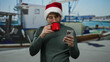 © Krakenimages.com - Man in christmas hat holding mug and smartphone at port with boats in background enjoying holiday season outdoors.