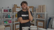 © Krakenimages.com - Hispanic man talking on phone in volunteer room surrounded by donation boxes and supplies, displaying a thoughtful expression.