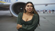 © Krakenimages.com - Woman smiling with arms crossed over cleavage in green blouse beside airplane engine on tarmac at airport with passengers boarding in background; confidence.
