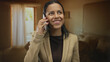 © Krakenimages.com - Woman, hispanic, smiling, talking on a phone, indoors, wearing a beige blazer, with brown interior lighting in a cozy room, expressing happiness and engagement.