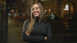© Krakenimages.com - Woman with arms crossed smiling and winking inside a cathedral interior wearing black turtleneck and long hair; confidence.