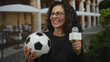 © Krakenimages.com - Woman reporter holding microphone and soccer ball at outdoor restaurant terrace capturing engaging sports news in vivid detail.