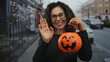 © Krakenimages.com - Middle age hispanic woman holds pumpkin basket and waves to camera on street; festivity celebration holiday fun.