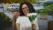 © Krakenimages.com - Woman holding bouquet and ring box, smiling on a vibrant street, showcasing a joyful engagement moment.