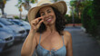 © Krakenimages.com - Woman in bikini and hat smiling outdoors on street with parked cars and palm trees in background, expressing smallness with her fingers.