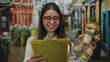© Krakenimages.com - Woman smiling with glasses holds toy and clipboard on vibrant street background, capturing cheerful outdoor scene with hispanic cultural elements and youthful energy.