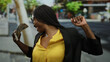© Krakenimages.com - African woman with curly hair smiling and holding us dollars outdoors in an urban city street, expressing happiness and confidence.