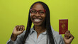 © Krakenimages.com - Smiling woman with braids wearing red glasses holding polish passport against yellow background.