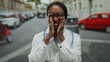 © Krakenimages.com - Woman stands smiling in city street wearing white lab coat with stethoscope vibrant urban environment bustling road big smile professional attire medical glasses