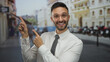 © Krakenimages.com - Hispanic man in white shirt and tie expressively pointing in an urban city street setting with blurred buildings and people in the background, wearing glasses and appearing surprised.