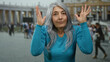 © Krakenimages.com - Elderly woman with grey hair gestures expressively in vibrant blue sweater, standing in bustling san pedro square at vatican, surrounded by blurred crowd and historic architecture.