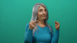 © Krakenimages.com - Senior woman with grey hair confidently gesturing middle finger against isolated green wall background in defiant casual expression.
